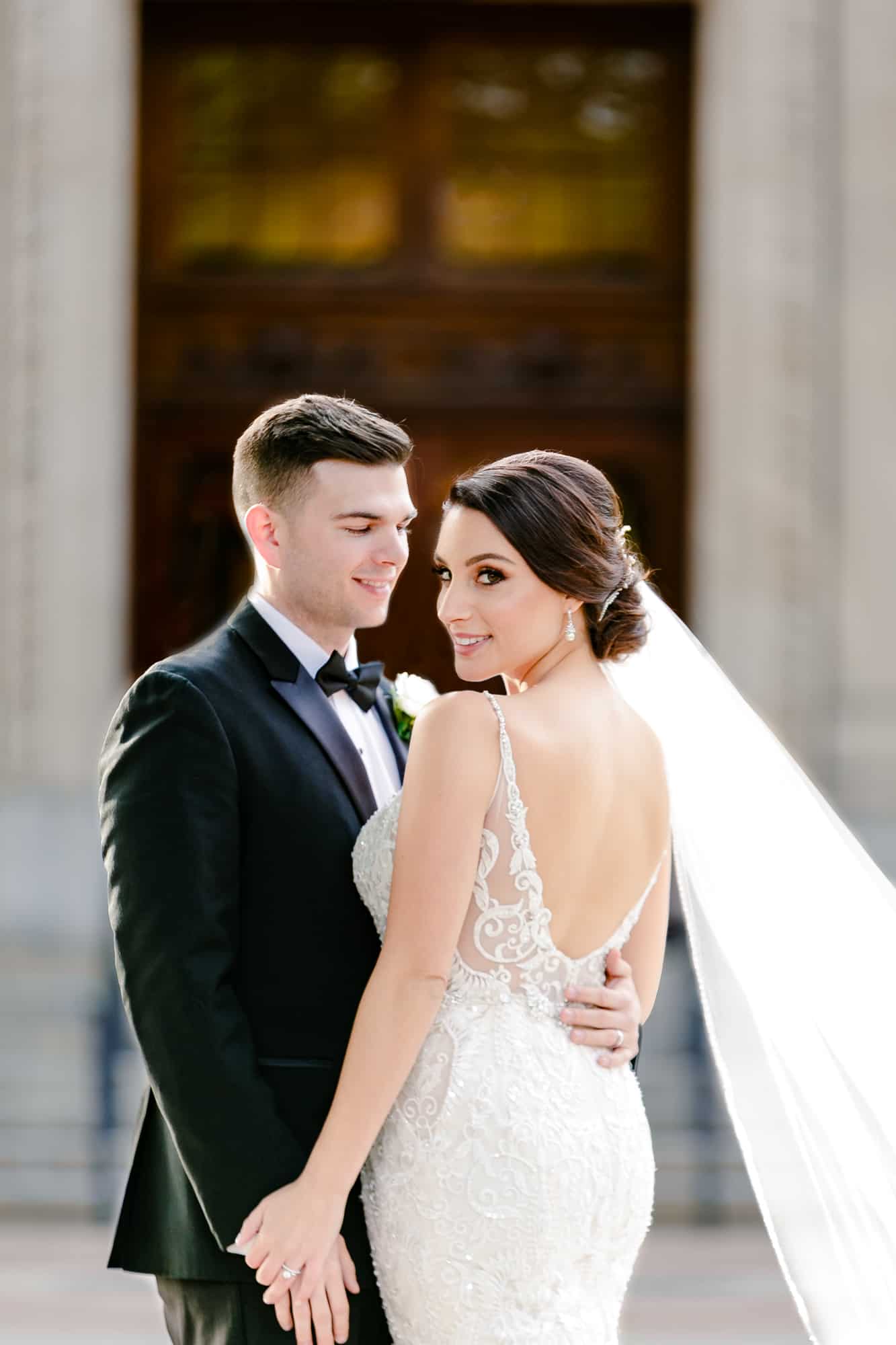 groom looking at bride while touching hands in backless beaded wedding gown