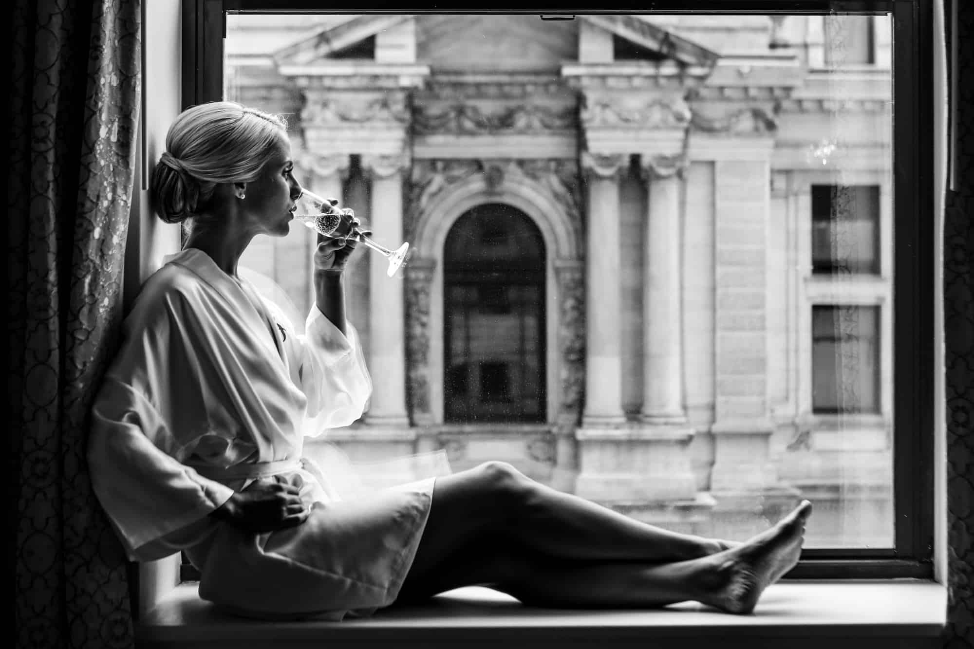 Bride drinking champagne in window overlooking City Hall at the Ritz Carlton Philadelphia