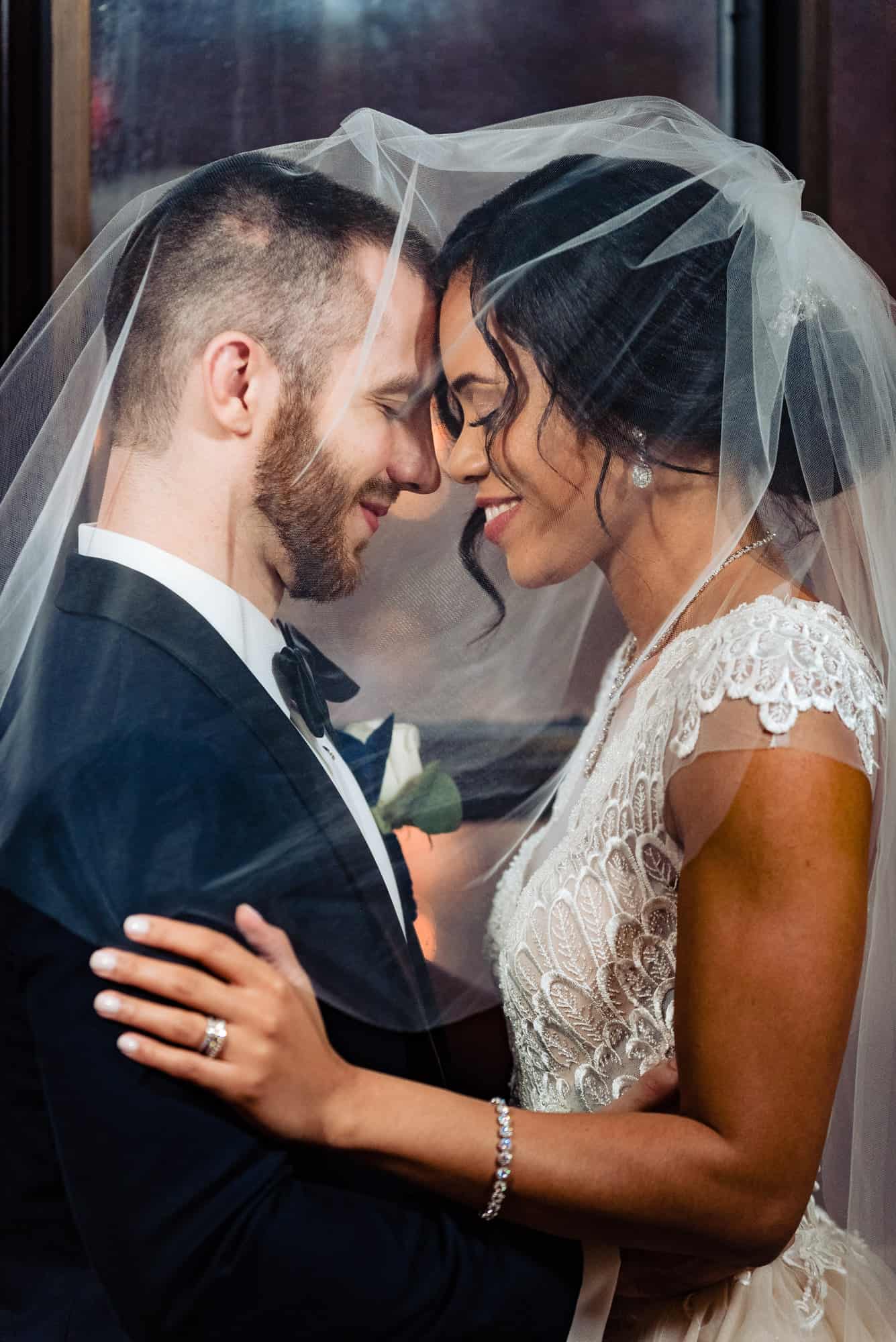 Bride and groom underneath a veil embracing