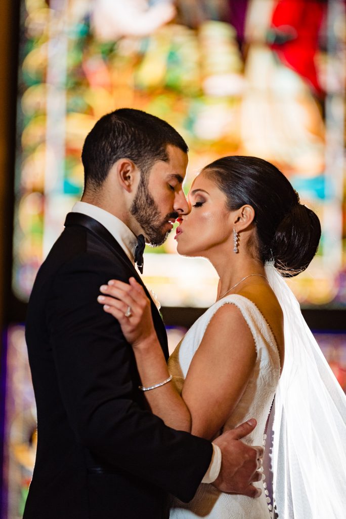 Bride and groom kiss in front of stained glass window