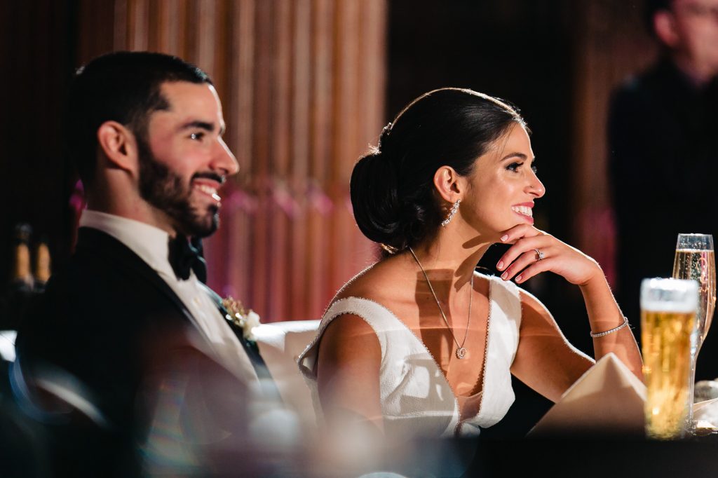 Bride and groom smiling during reception speeches.