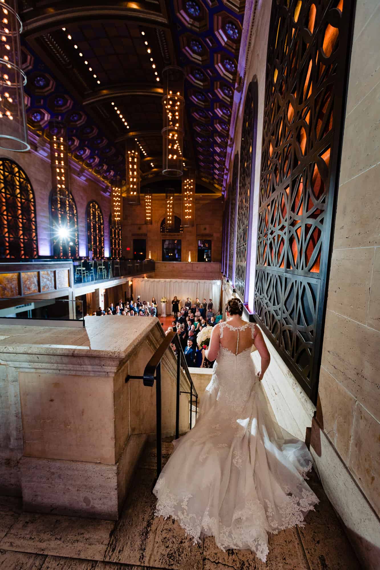 bride walking down the stairs back shot with everyone downstairs