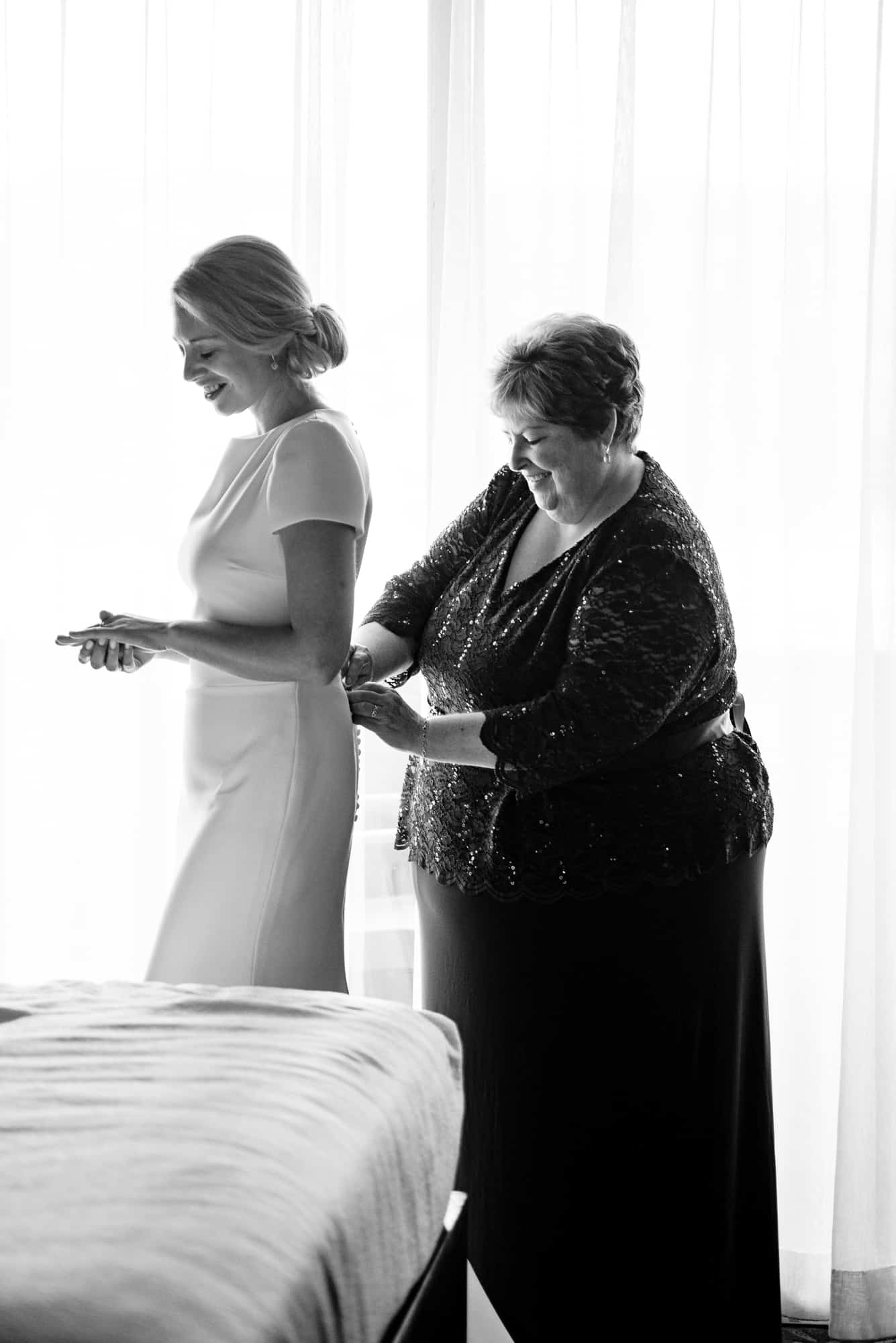 the bride's mother fixing the back of her wedding dress black and white shot