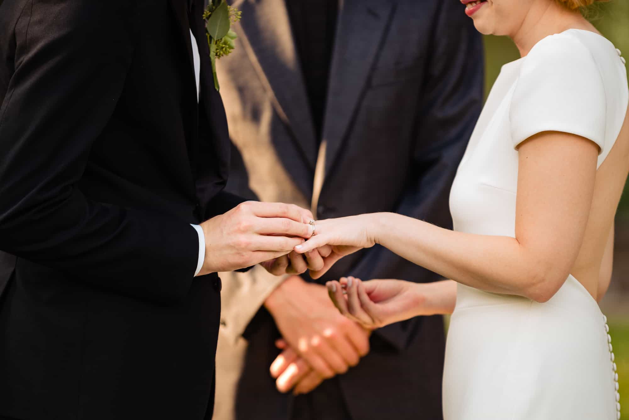 close shot of groom putting ring on brides finger during their Morris Arboretum Wedding Ceremony