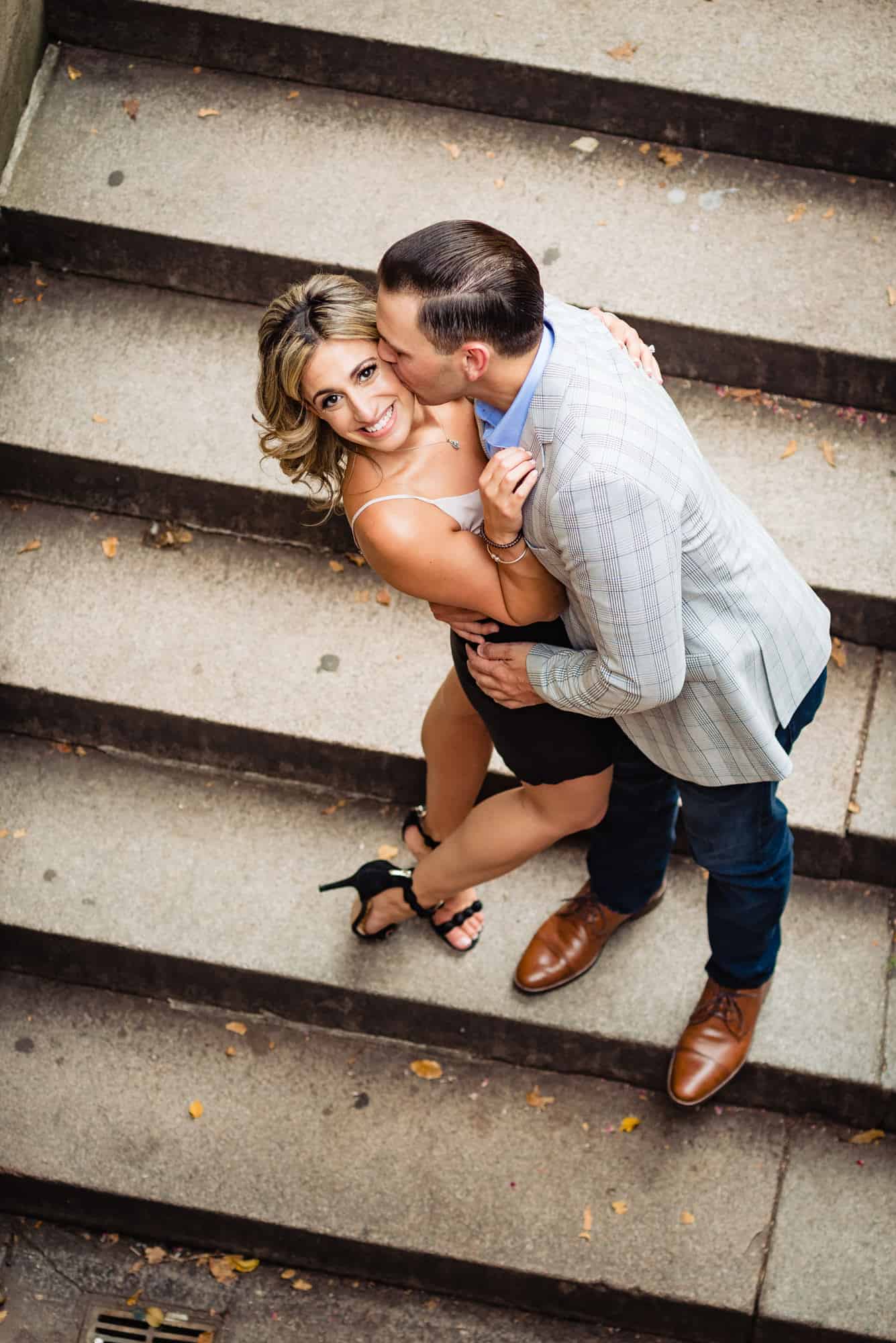 couple on steps embracing while female looks at camera eagle eye shot in central park