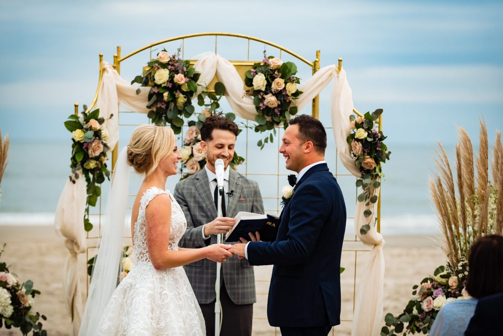 Bride and groom smiling at each other while holding hands in a beach wedding
