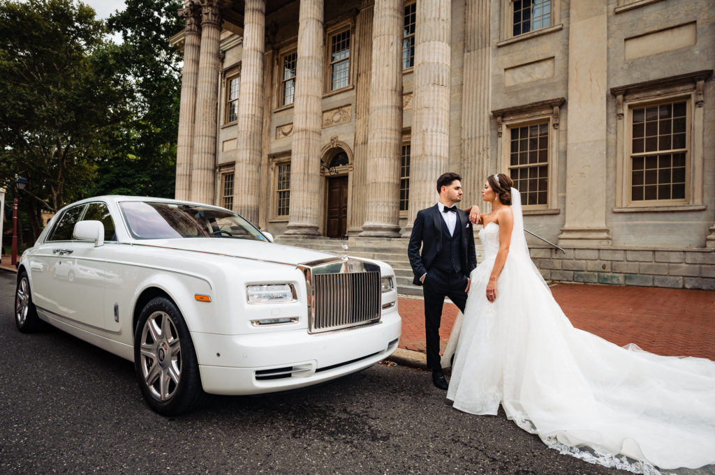 the newlyweds taking a pose beside their bridal car