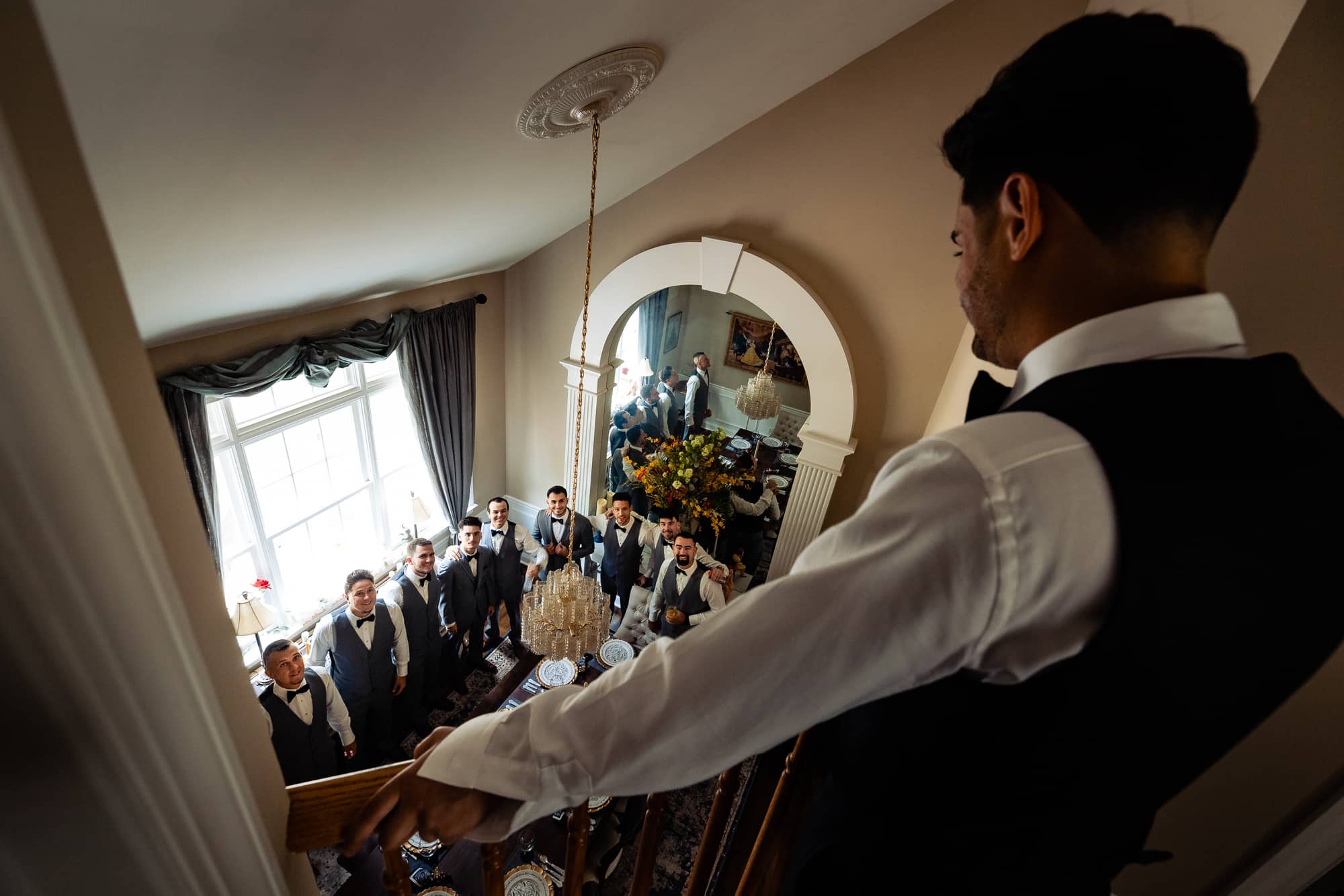 groom is looking down the stairs while entourage awaits