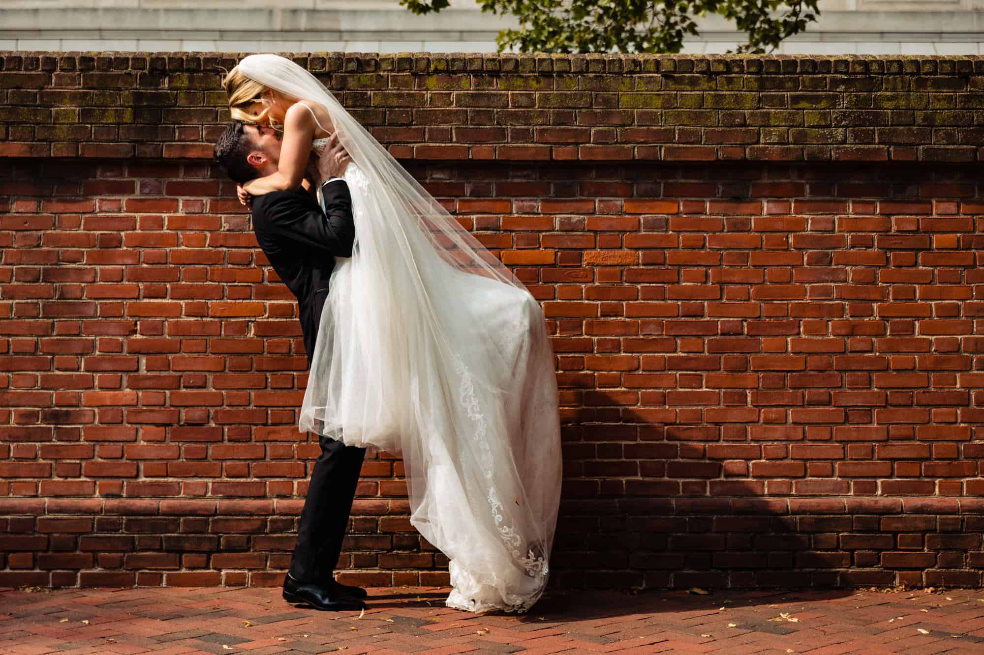 groom is carrying his bride while kissing her outside the church