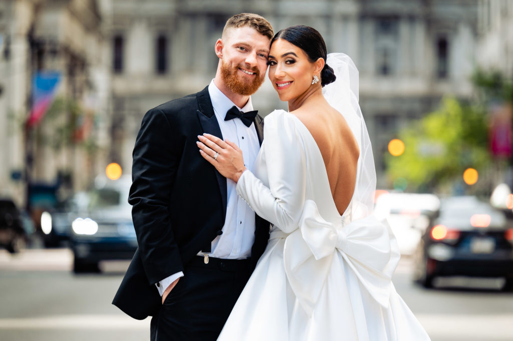 groom and bride poses for the camera in the middle of the city