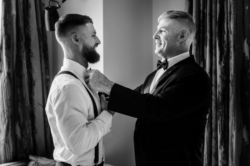 black and white shot of the groom's dad fixing his tie