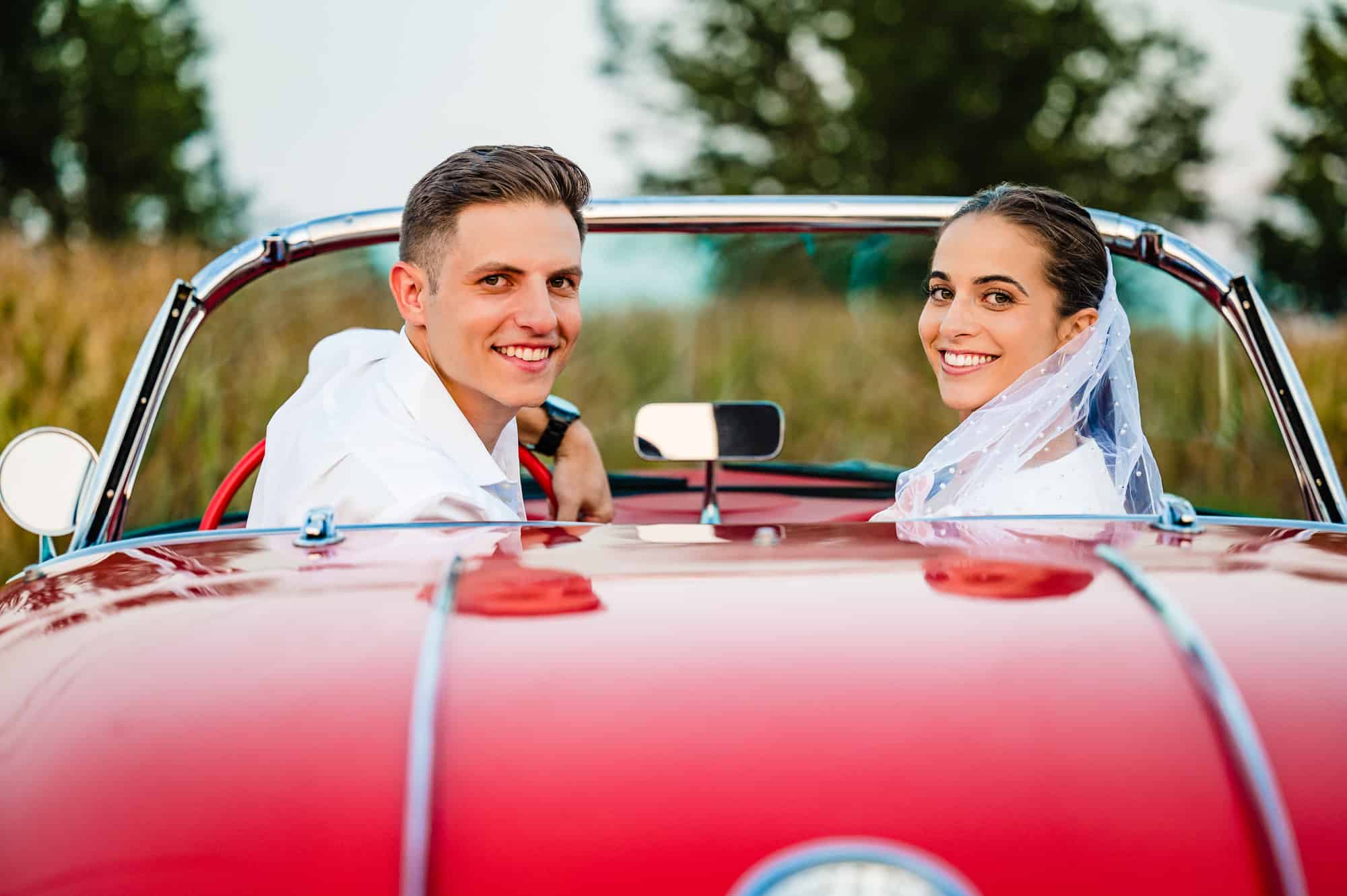 couple are all smiles for the camera while on the seat of their red 1958 Chevrolet Corvette roadster