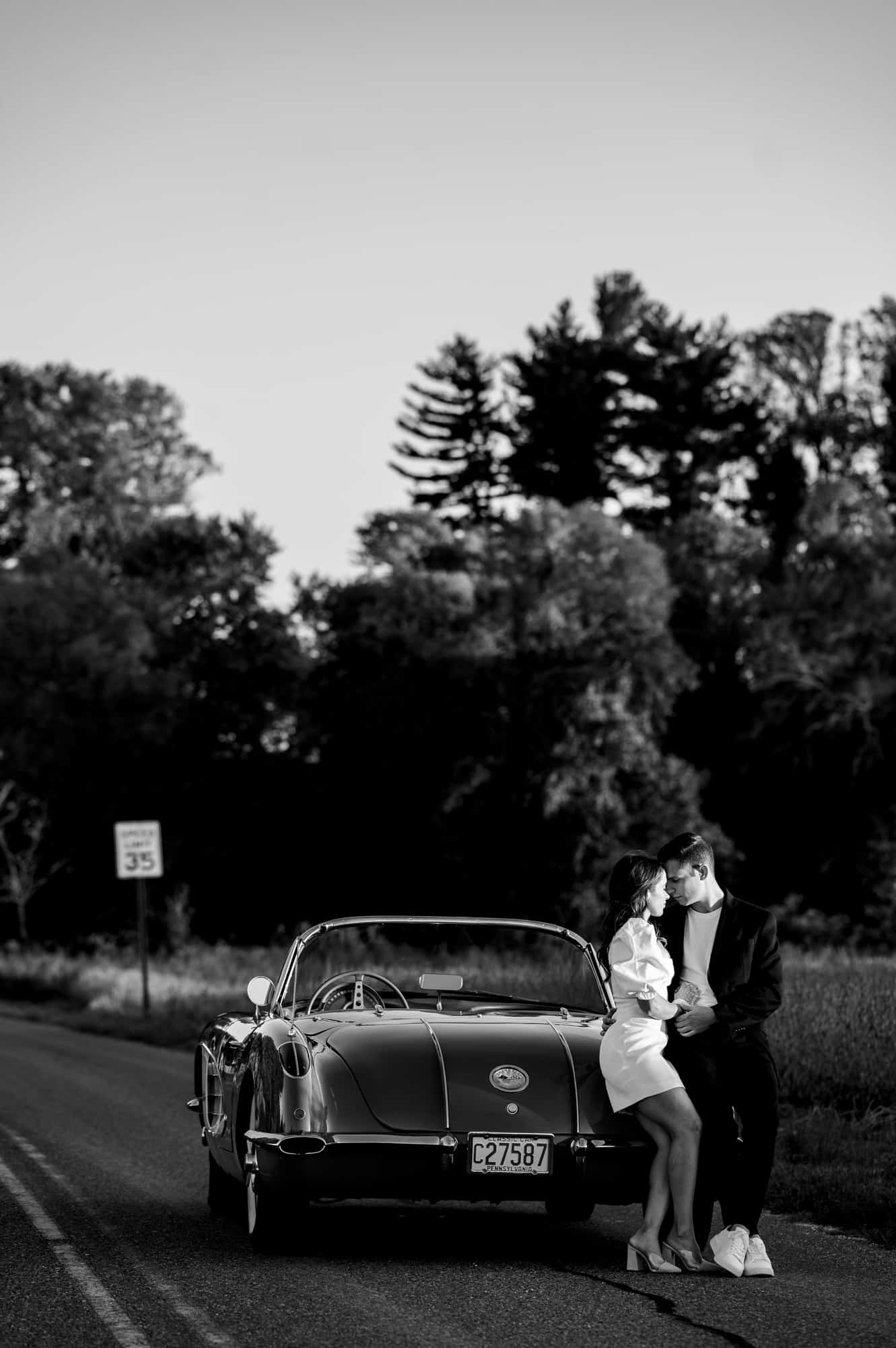 black and white shot of the couple taking a pose beside their vintage corvette