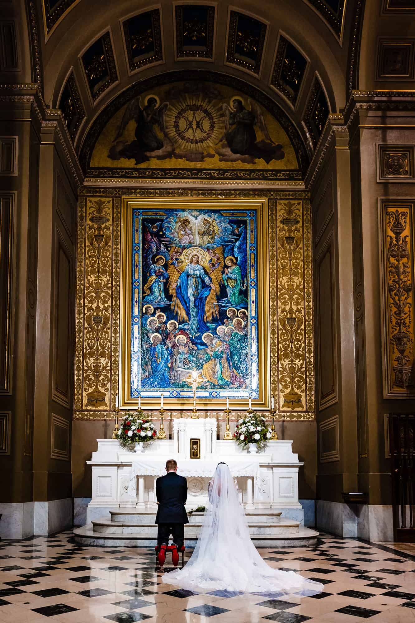 bride and groom kneeling in front of the altar