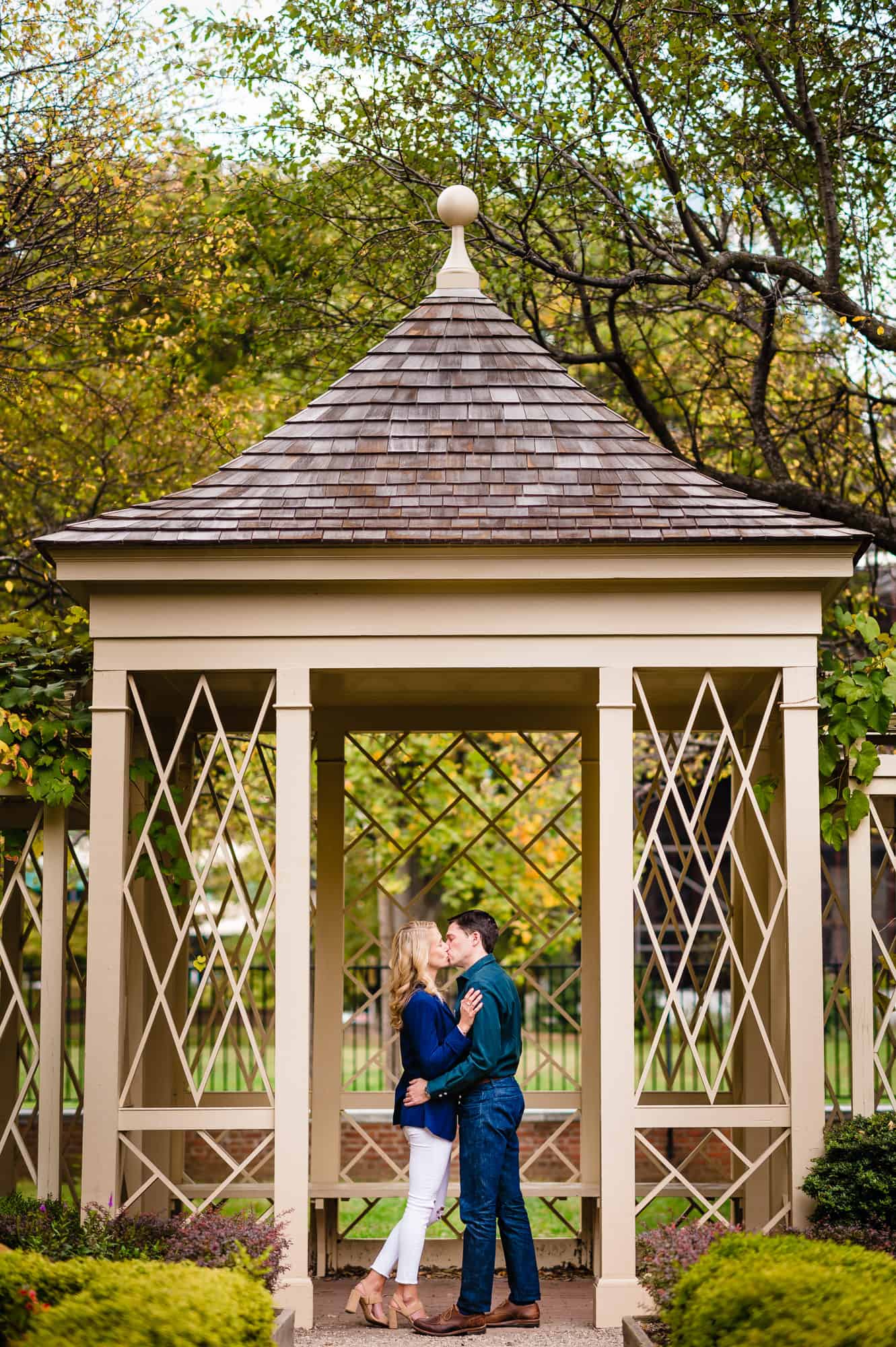 During their engagement photoshoot, the couple kisses under the gazebo at 18th Century Gardens