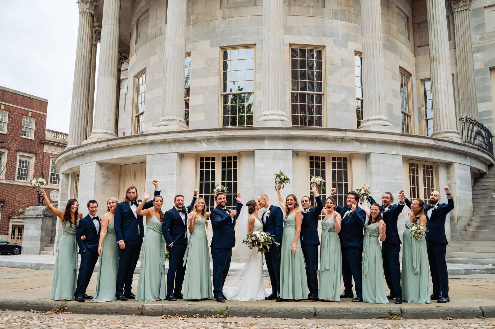 bride and groom kissing while the bridesmaids and groomsmen rejoices