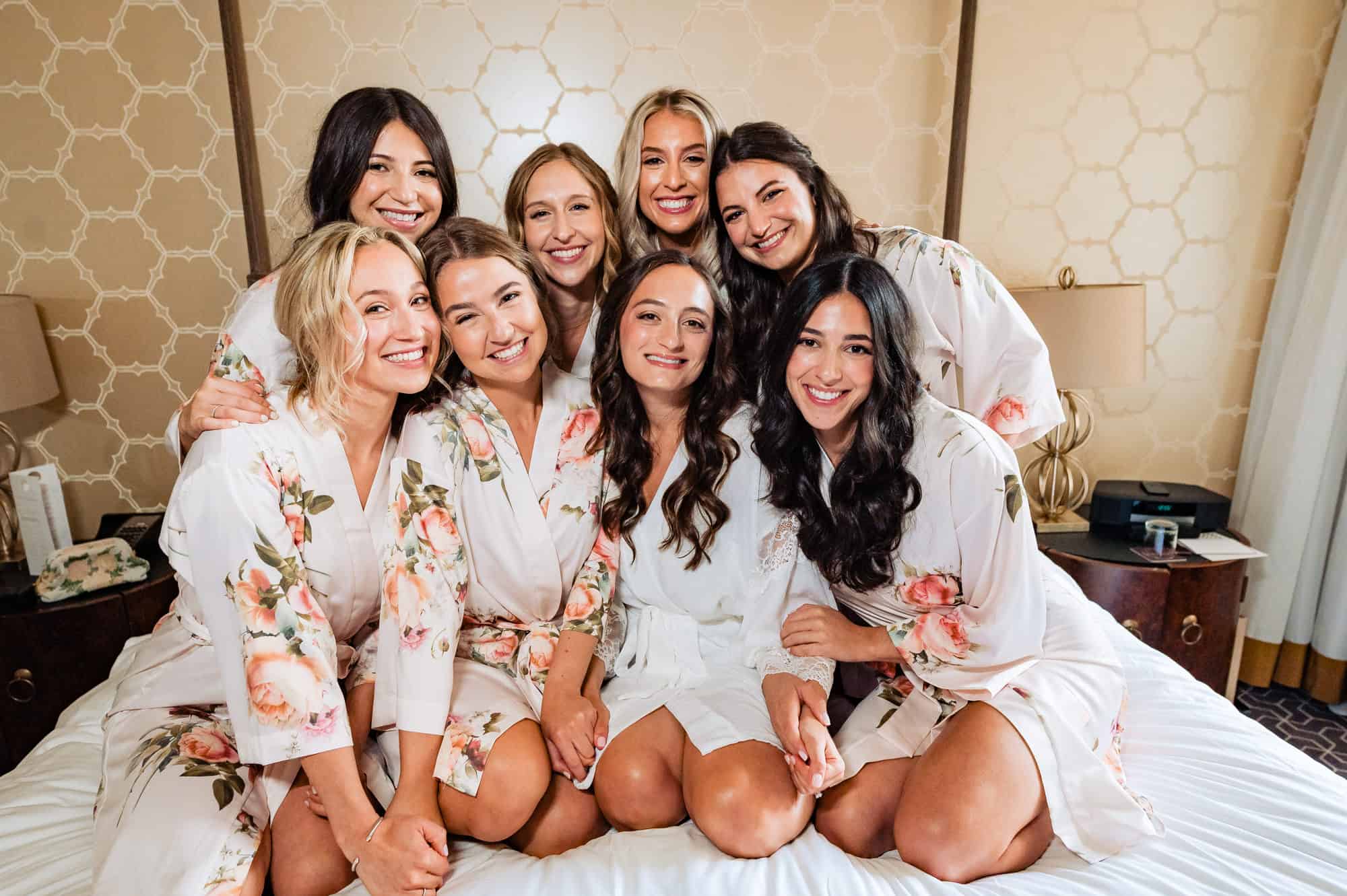 bride poses with her bridesmaids sitting on the bed in their sleeping robes before her rittenhouse hotel wedding