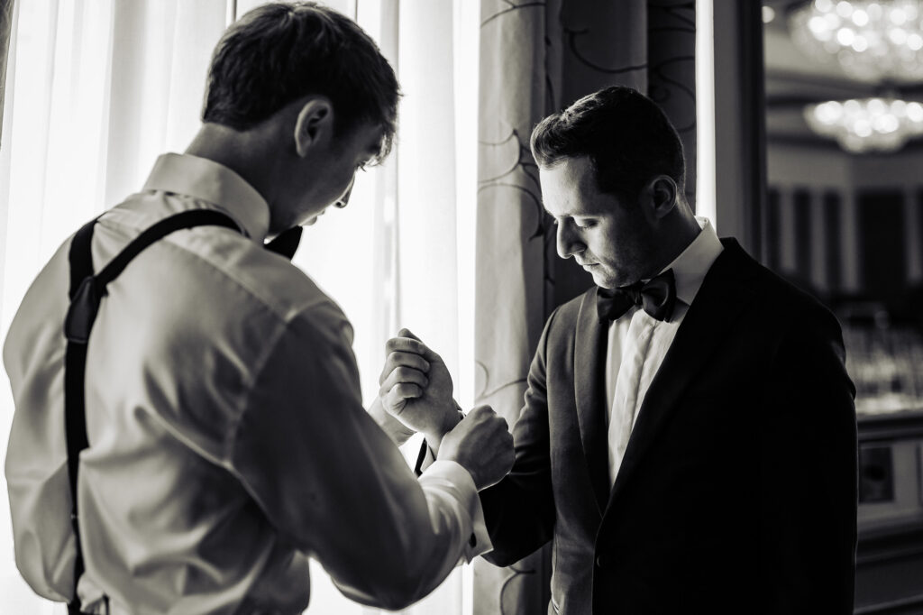 black and white shot of the groom getting ready with the help of his bestman
