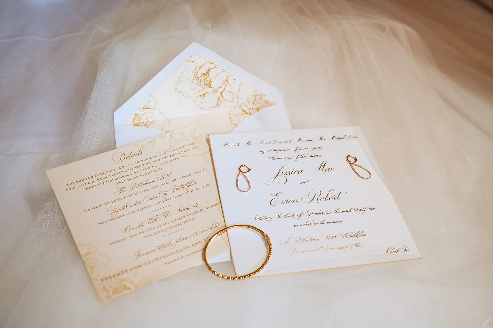 a wedding invitation with a gold bracelet placed on top of it