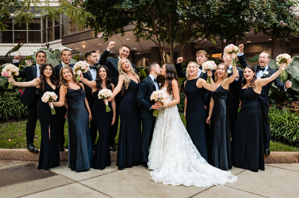 the newlyweds kiss while their bridal entourage cheer them