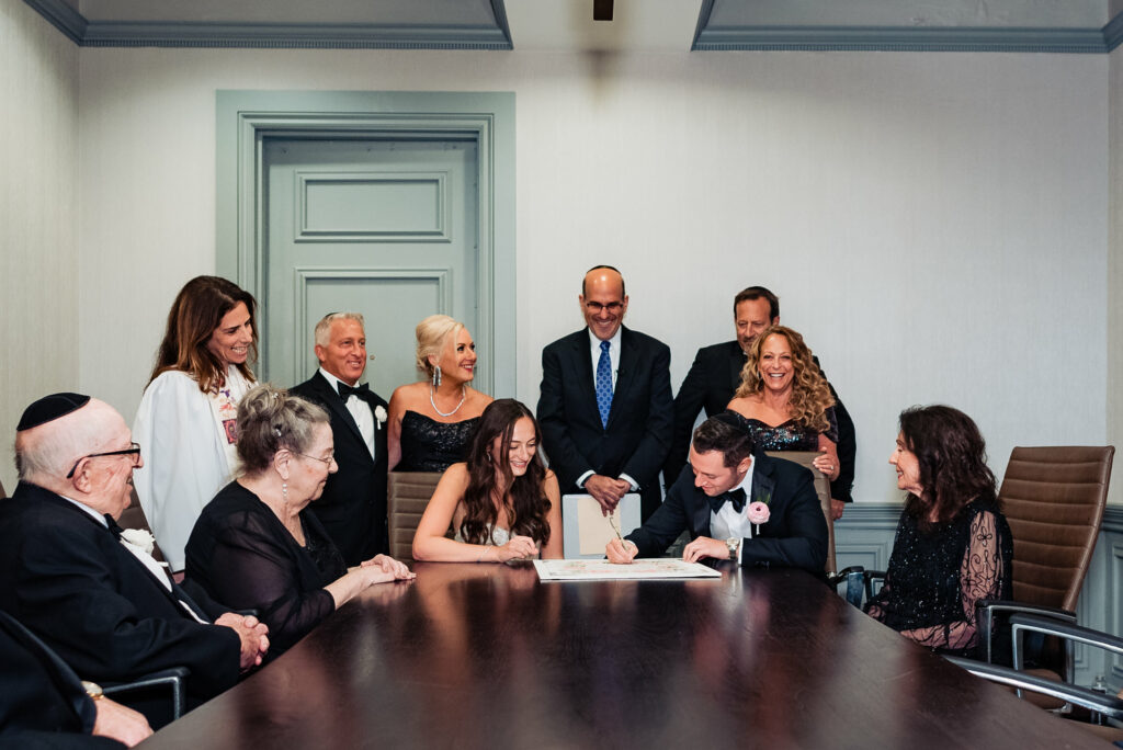 the newlyweds signing their marriage contracts while their family surrounds them