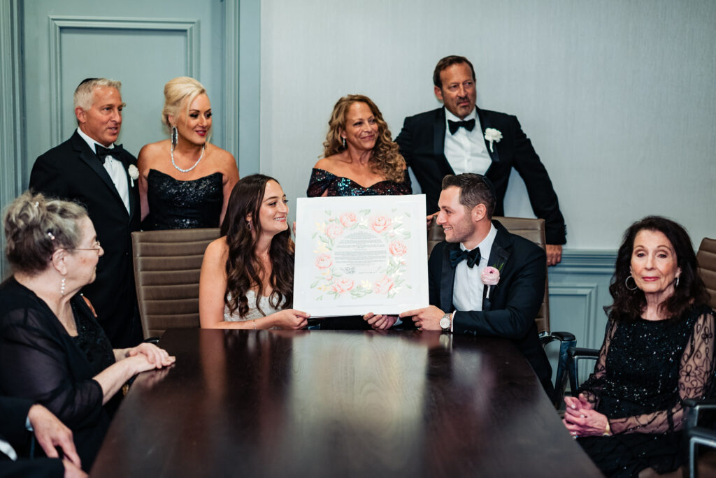 the newlyweds holding their ketubah while their family surrounds them