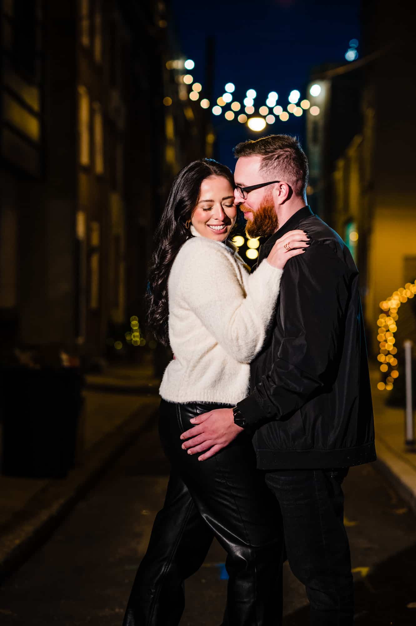 The couple smiles before the camera at night during their fun engagement shoot in south Philadelphia