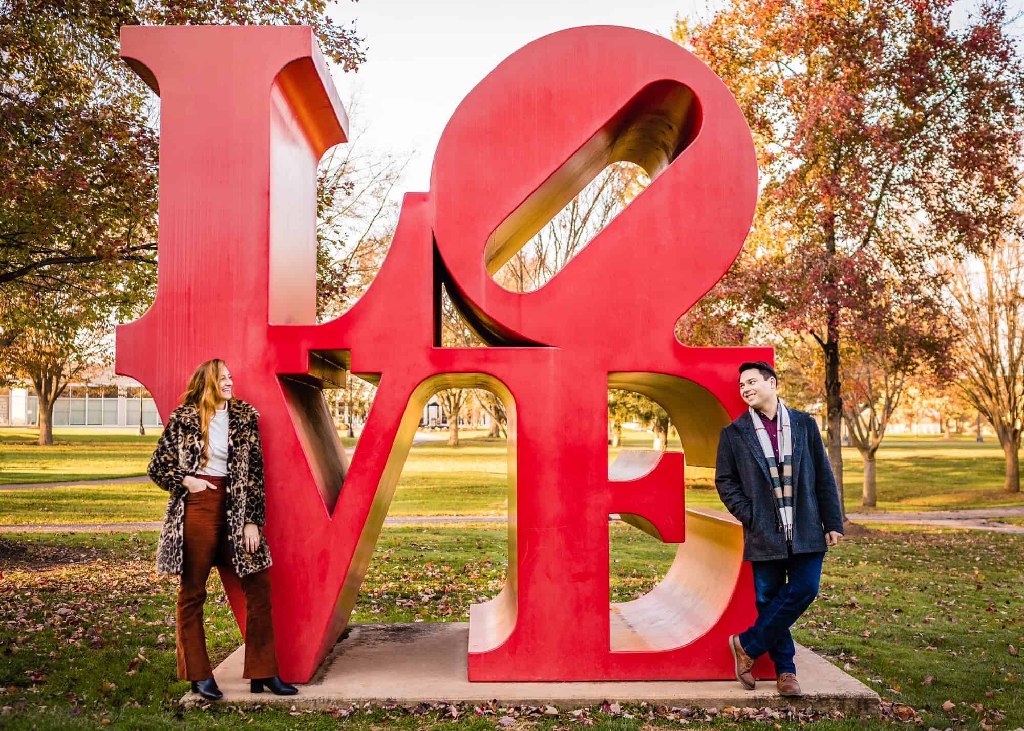 couple posing with the love sculpture designed by Robert Indiana located on the grounds of Ursinus College during their engagement photoshoot