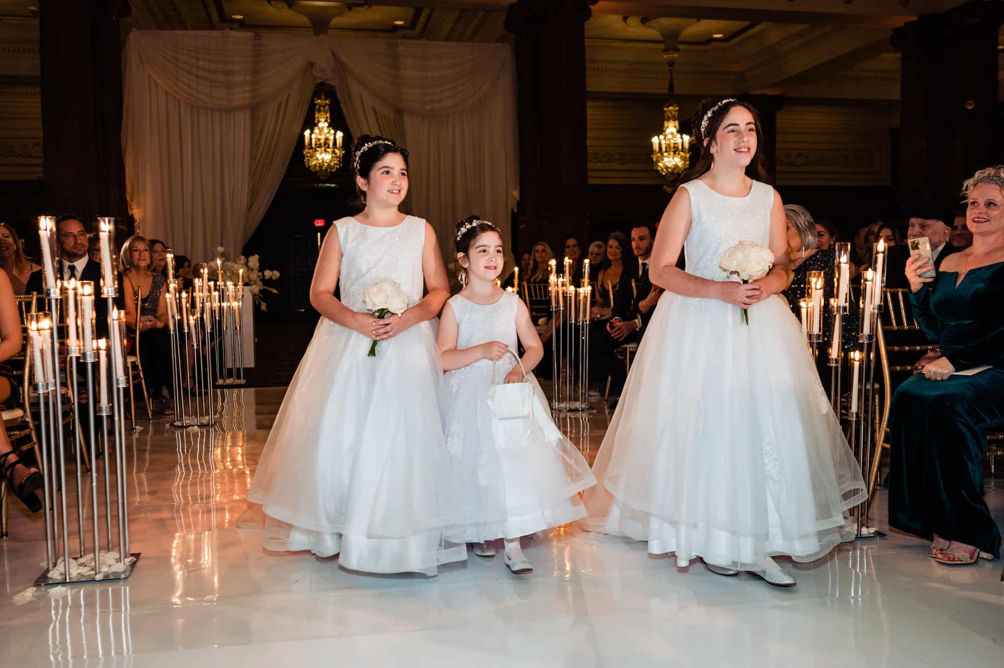 three flower girls in their white dress walking towards the altar