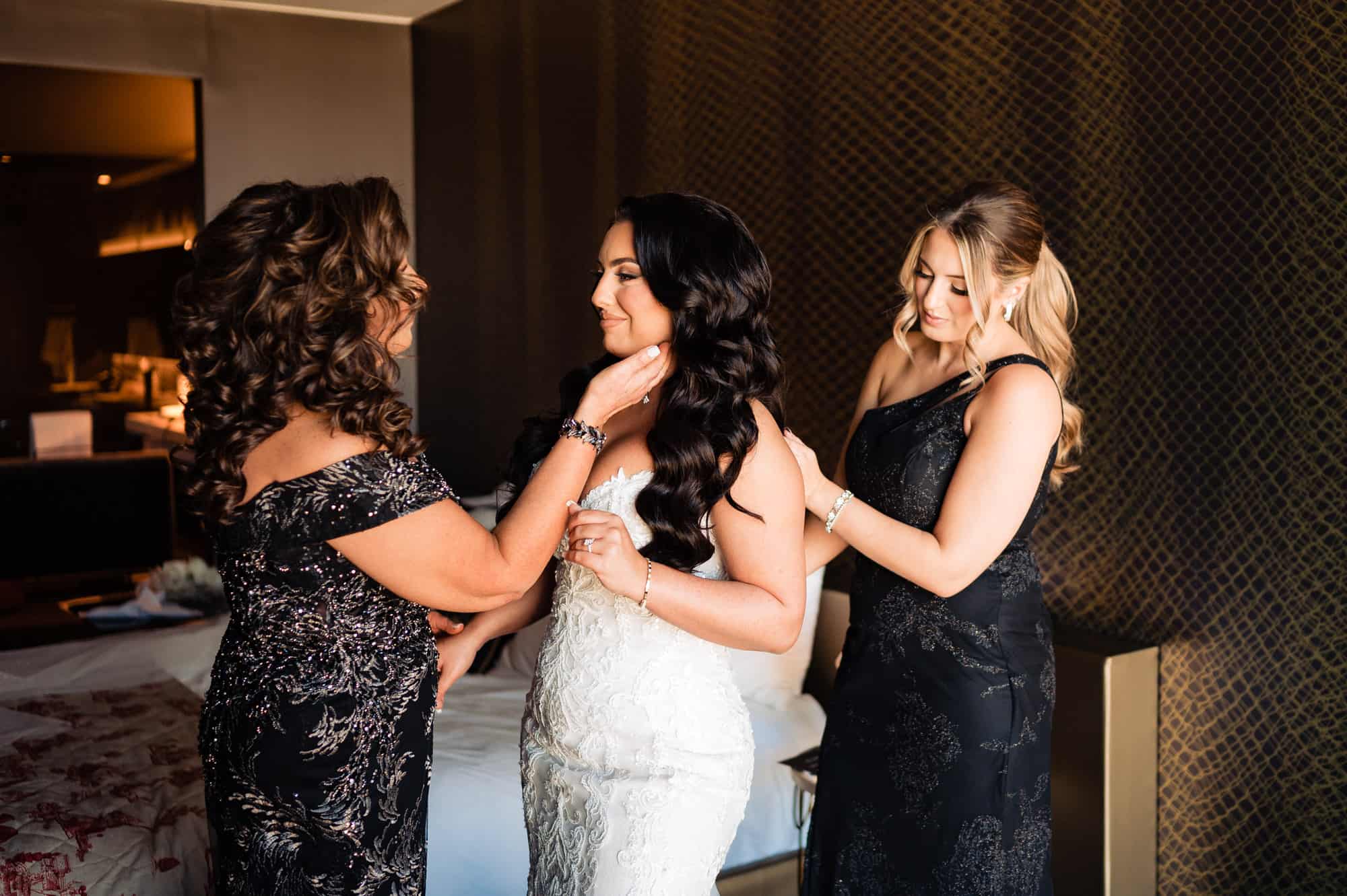 bride getting ready for her wedding with the help of her mother and sister