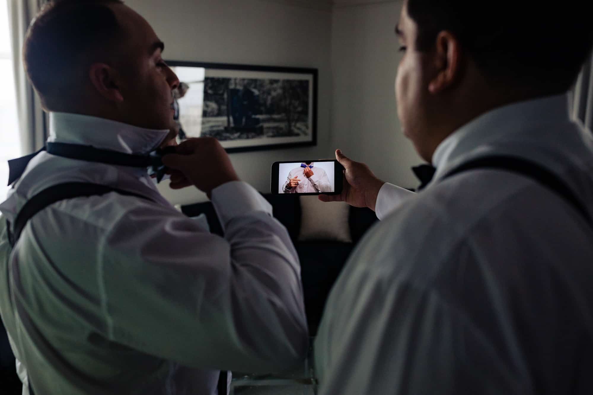 the groom and groomsman watching how to tie a tie on youtube