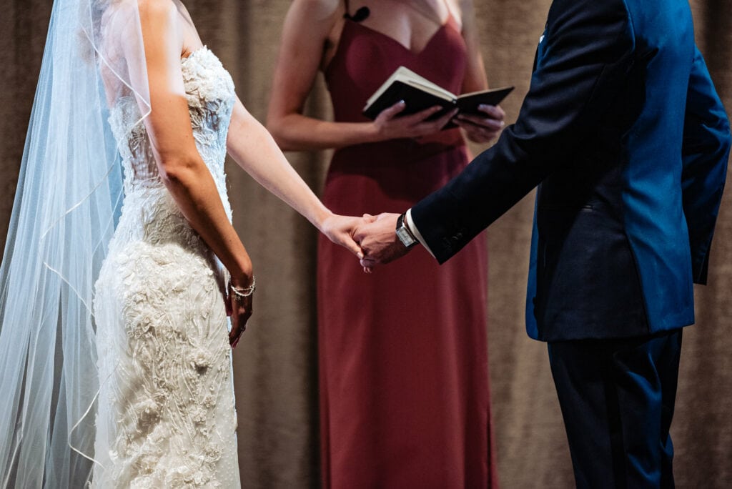 close up shot of the bride and groom holding each other's hand infront