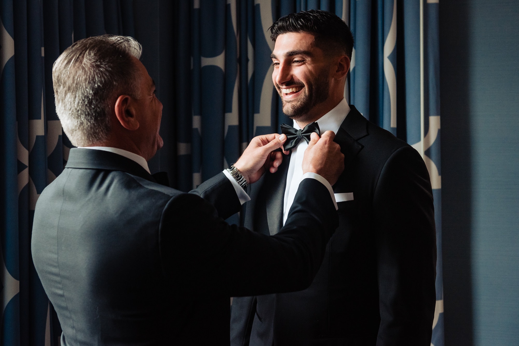 groom smiles while his dad puts on his tie