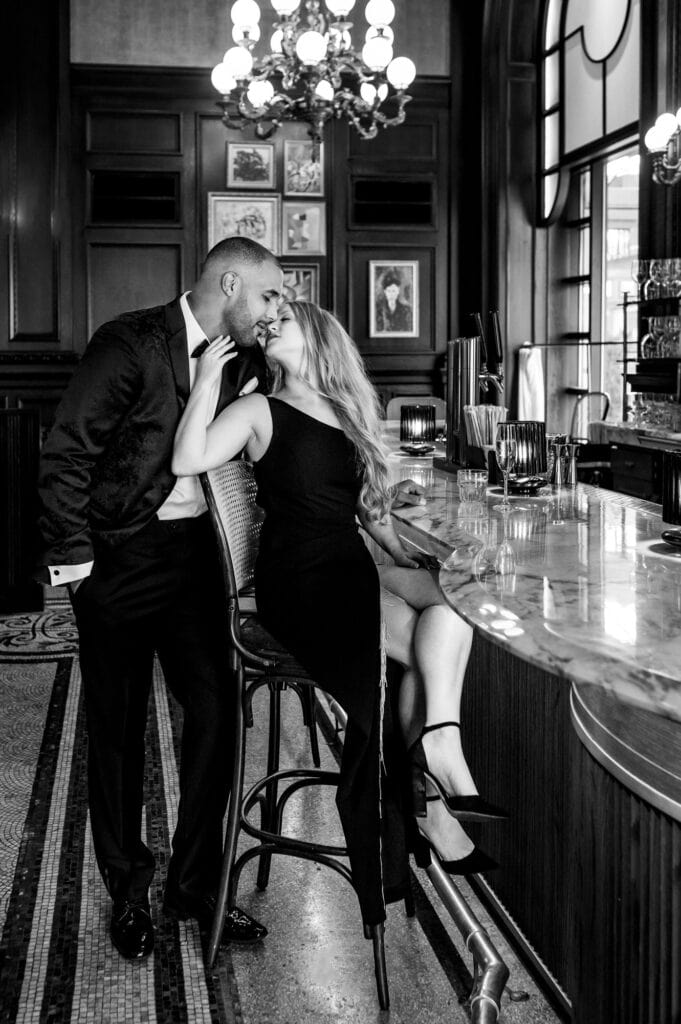 black and white image of couple shares a kiss at a bar counter during their Hotel DuPont Engagement Shoot