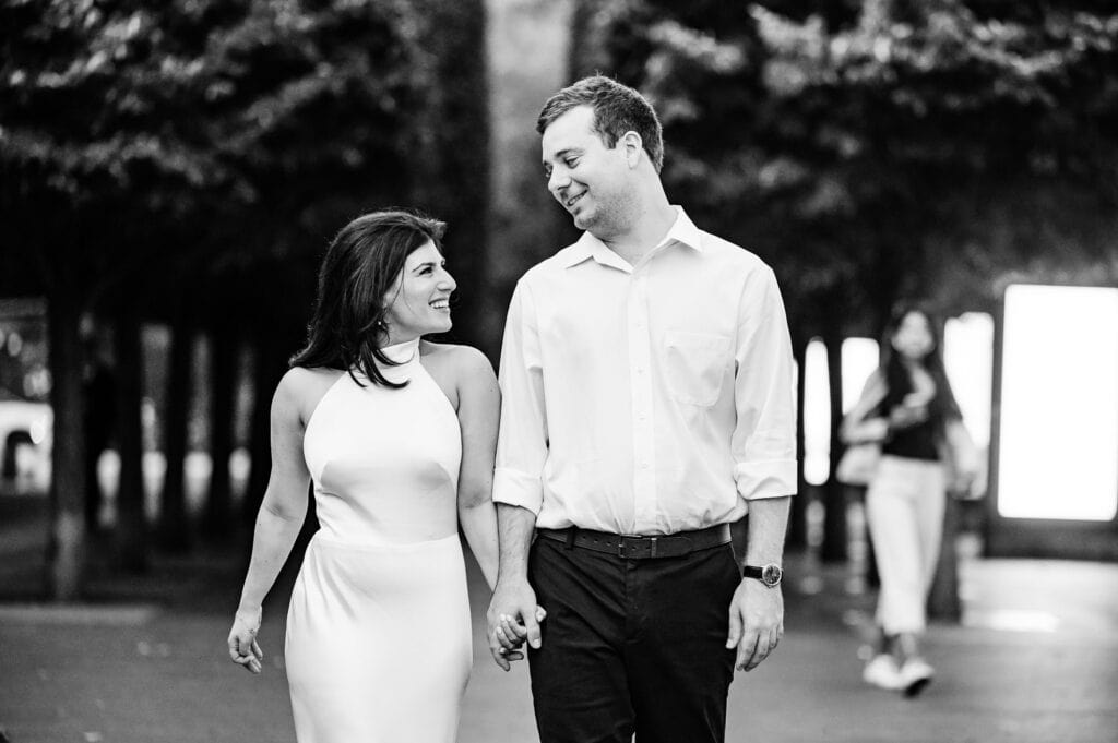 black and white shot of man and woman holding eachother's hand while looking at eachother as they walk