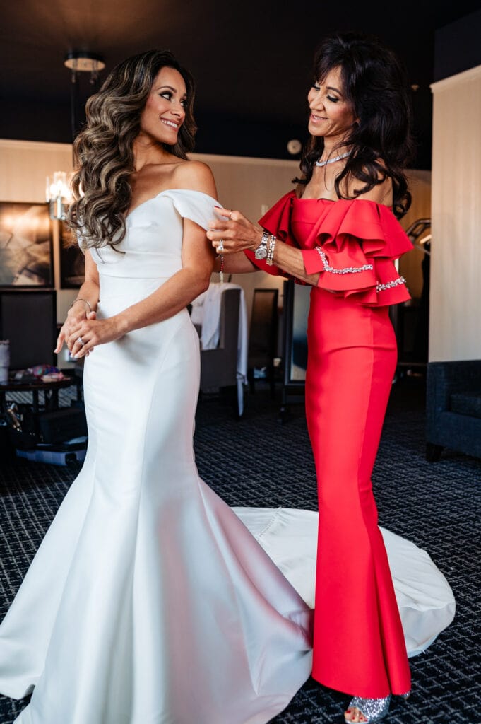 the bride in her wedding gown and maid of honor in her red gown, both smiling at each other