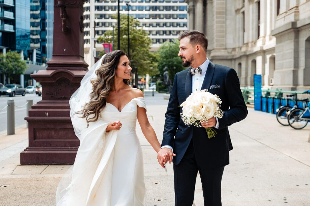 bride and groom looking at each other and holding hands while walking on the side walk