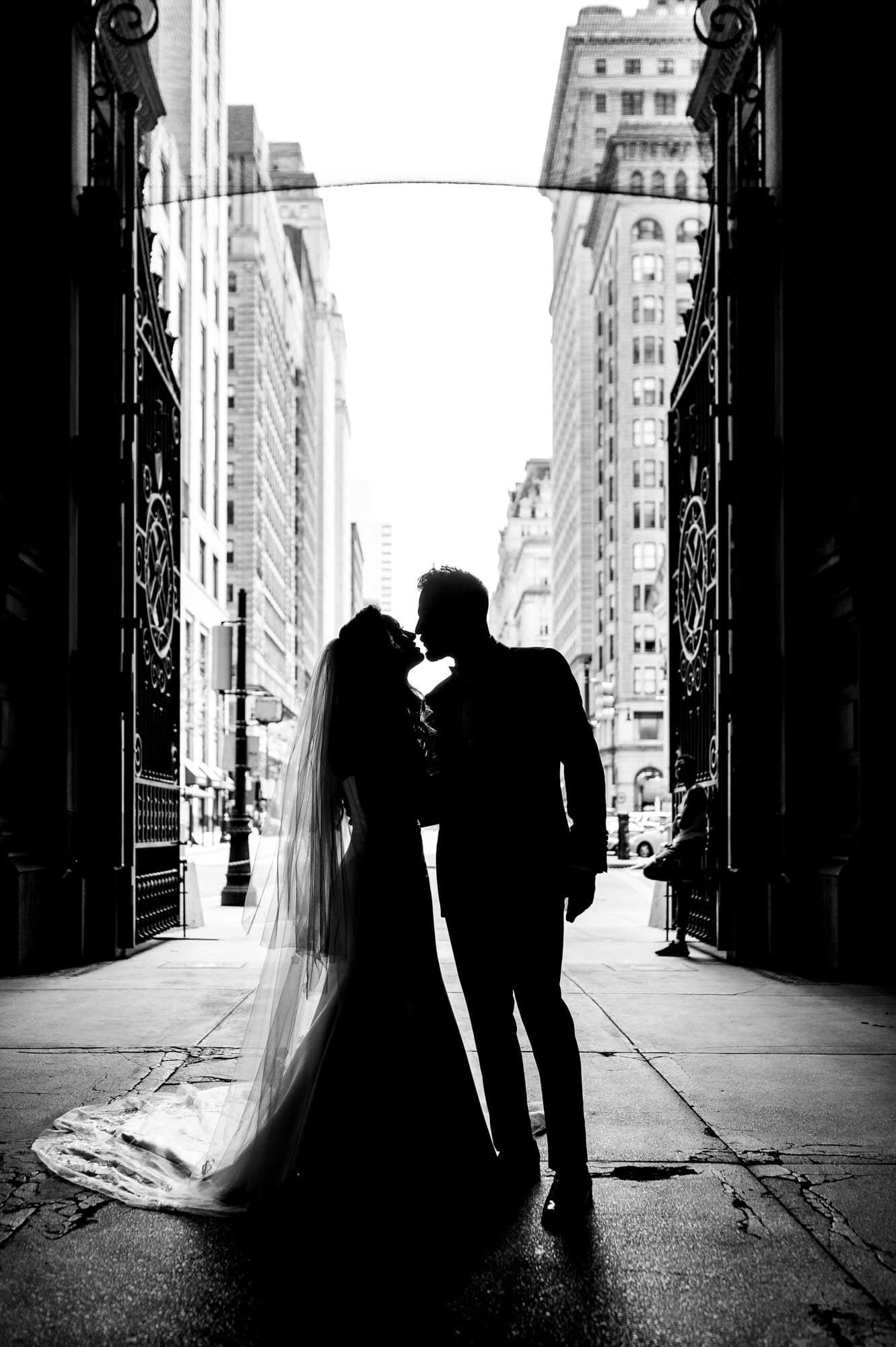 bride and groom share a tender kiss in a dark alley against the light background