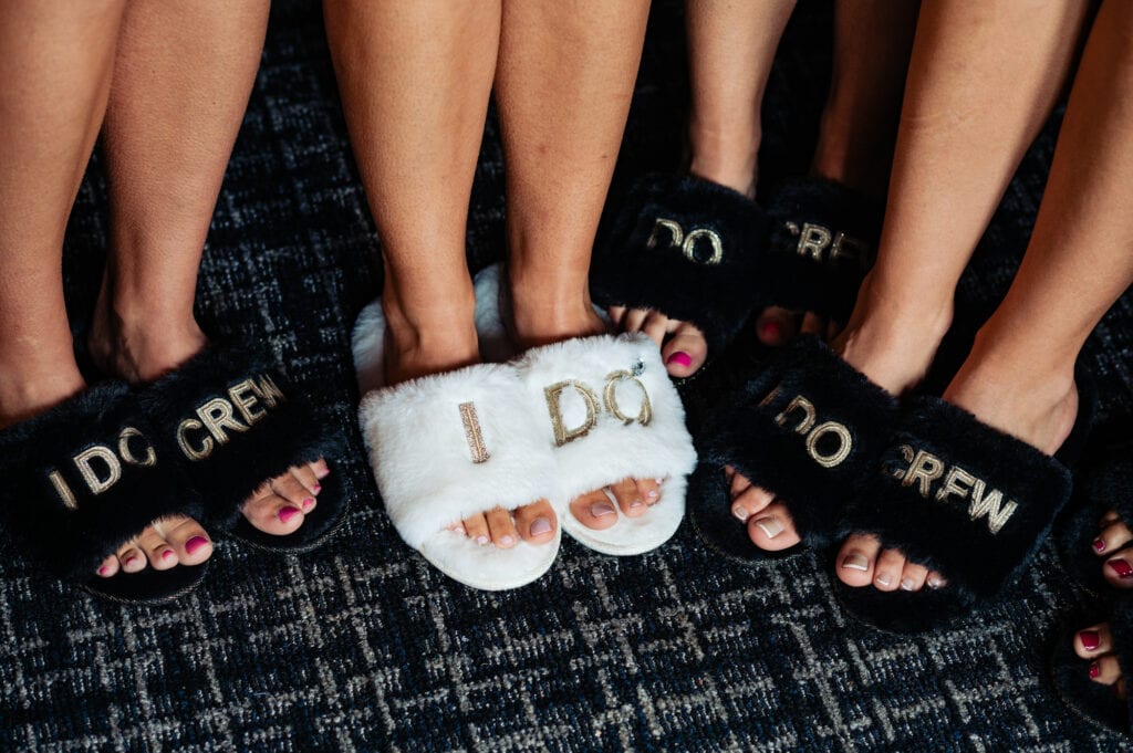 bride wearing her white colored fur slippers and the bridesmaids wearing their black colored fur slippers with the words "I do" and "I do crew"