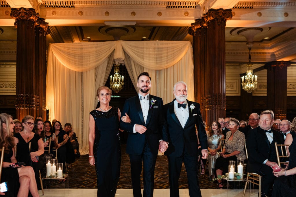 the groom's father and mother walking him on the aisle