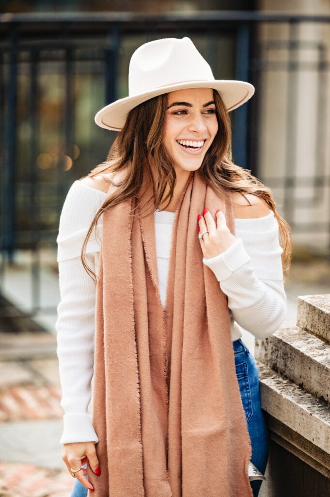 Woman in a white long-sleeved top and cap, sporting a brown shawl, radiates a joyful smile, capturing the essence of a cherished moment