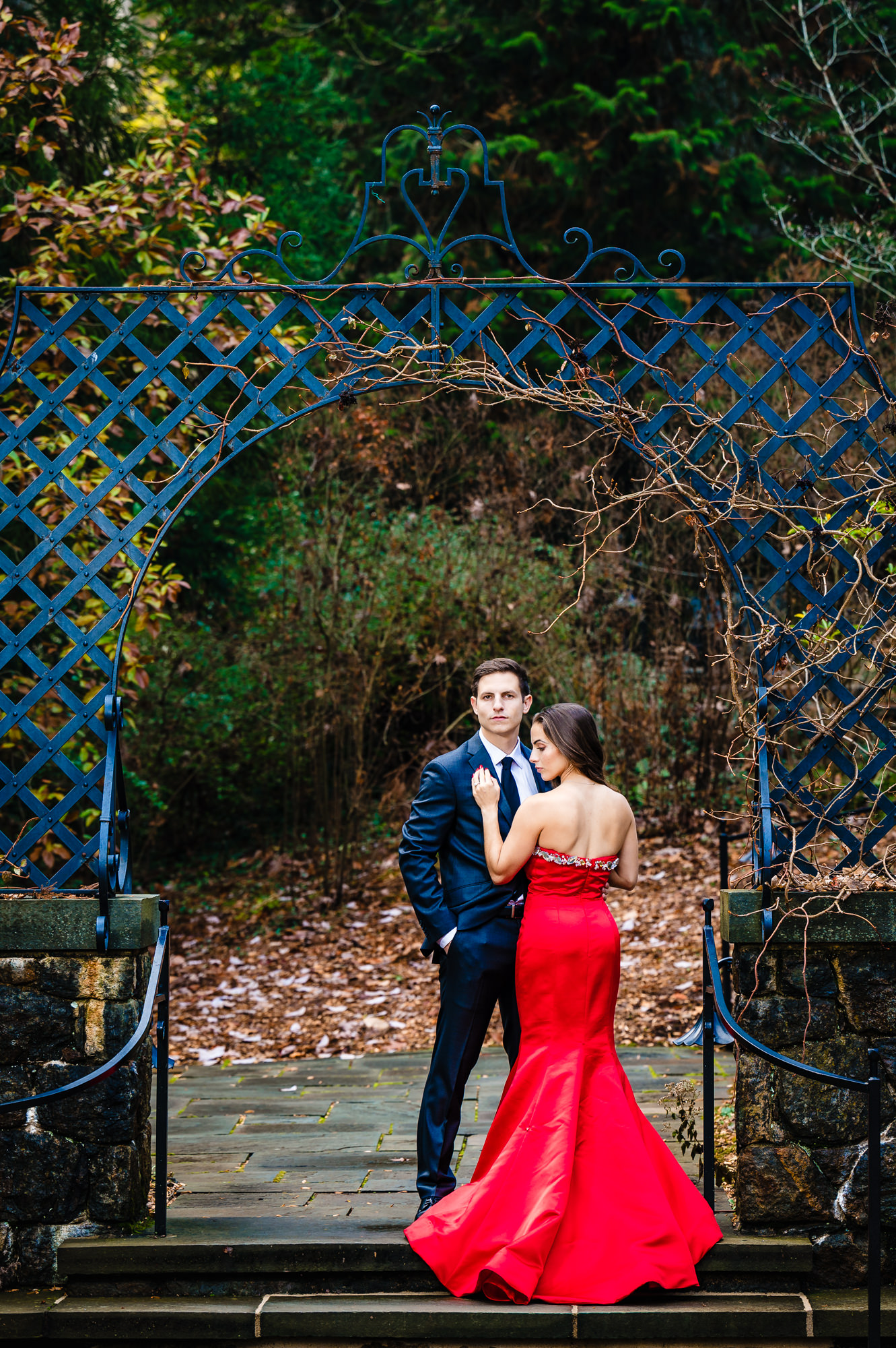 An engaged couple cherishing an intimate moment in a warm embrace amidst the vibrant fall foliage. Sun rays filter through the colorful trees surrounding them, leaves cascading down during their sweet autumn photo shoot.