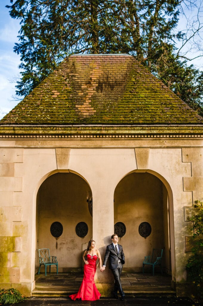 Amid Winterthur garden's vivid autumn colors, an engaged couple strikes a delightful pose, enveloped by the elegance of an arch structure, celebrating their profound love.