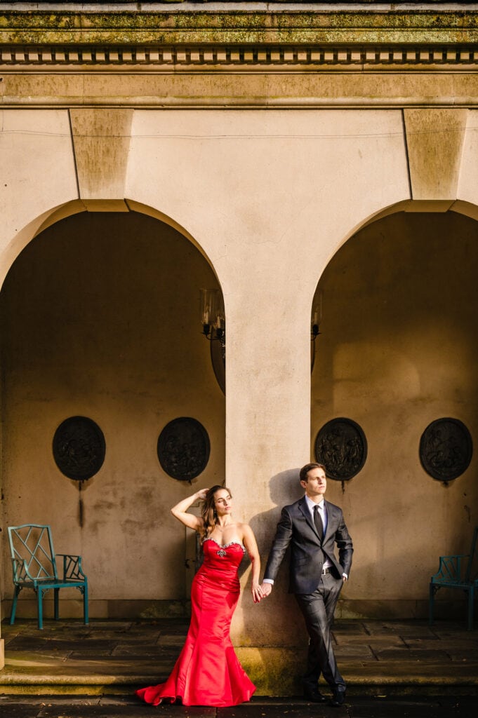 Amid Winterthur garden's vivid autumn colors, an engaged couple strikes a delightful pose, enveloped by the elegance of an arch structure, celebrating their profound love.