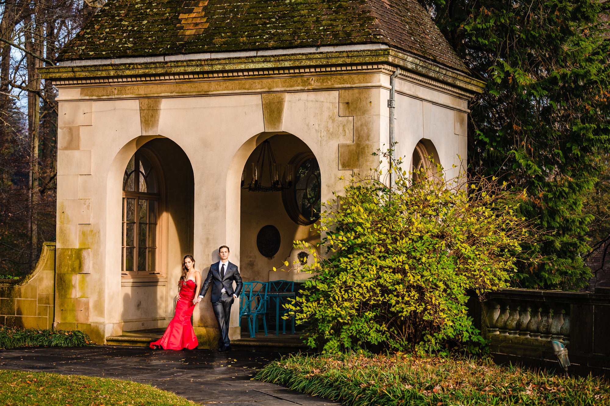 In Winterthur garden's vivid autumn hues, an engaged couple looks at the camera, framed by the beauty of an elegant arch structure, celebrating their love during their winterthur engagement photoshoot