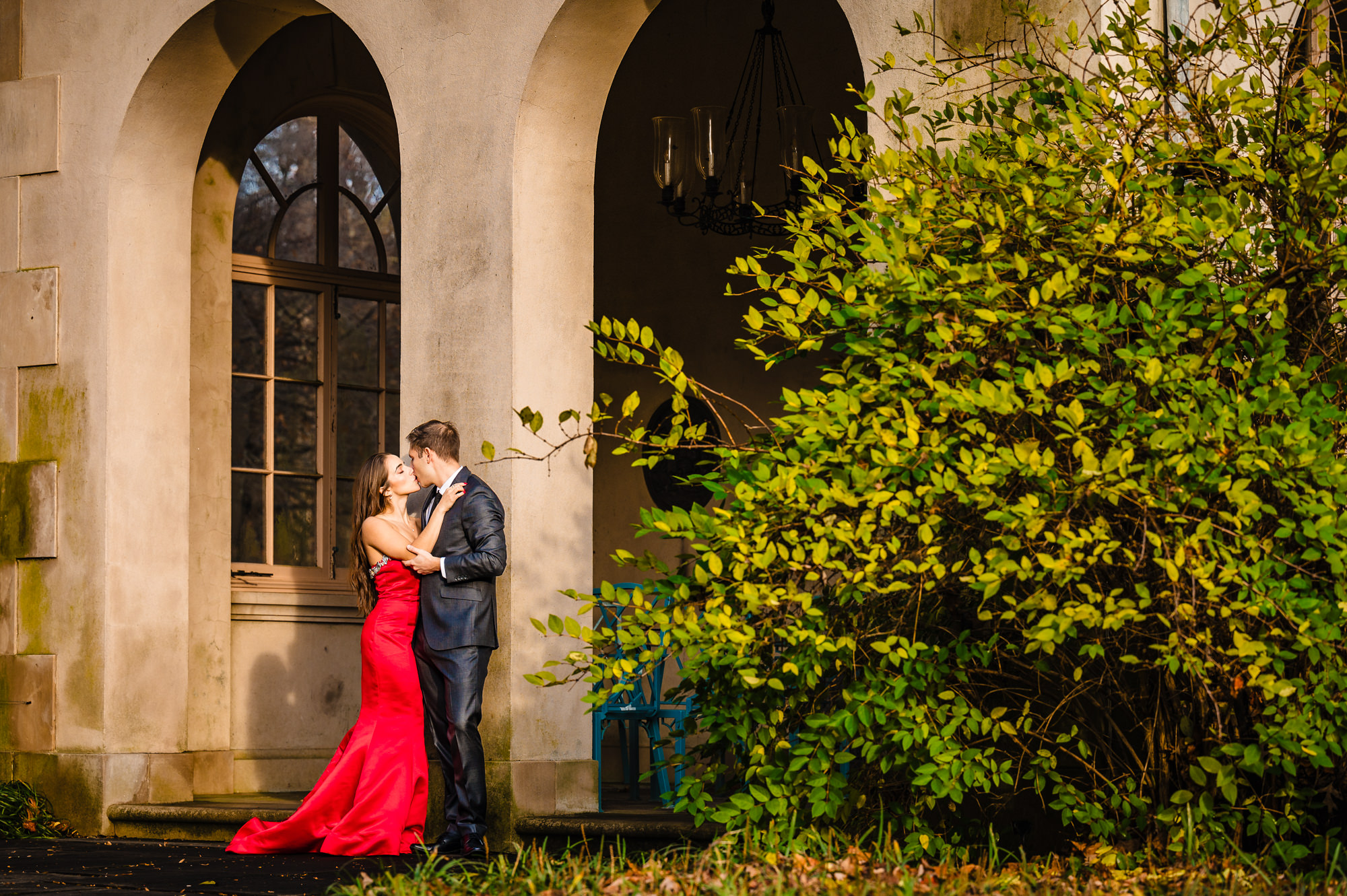 Amidst Winterthur garden's vibrant fall tones, a tender kiss between a loving couple takes center stage against the backdrop of an elegant arch structure.