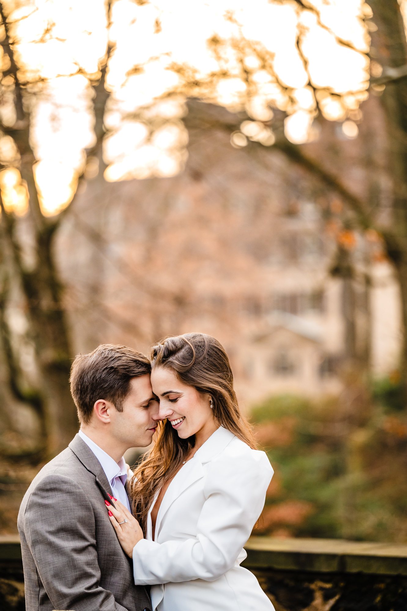 A bride-to-be smiles brightly, her eyes crinkled in joy, as her fiancé affectionately presses his cheek against hers.