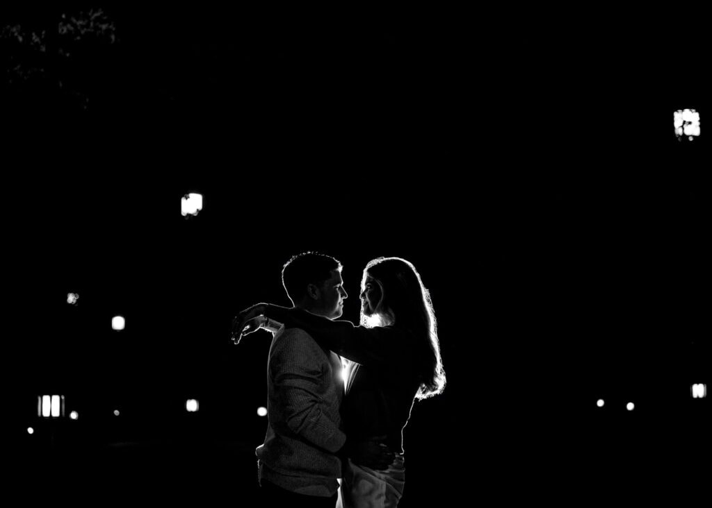 black and white night shot of couple facing each other, woman's arms on the man's shoulders while the man's hands is on her hips