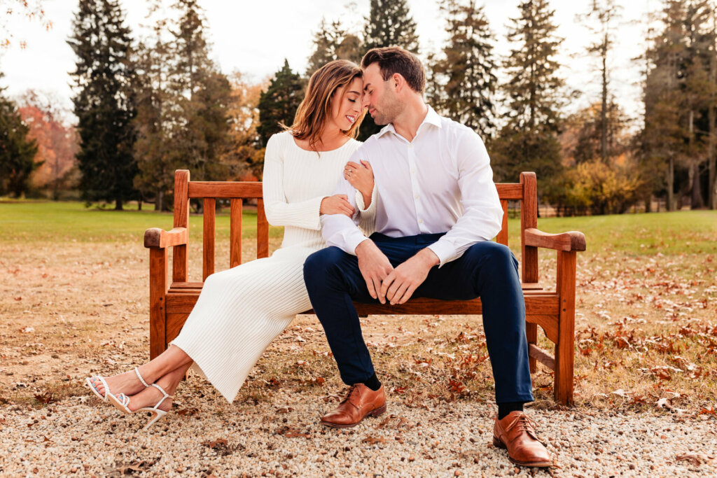 Charming pose as a man and woman sit on a bench, leaning their foreheads on each other in a sweet moment. Their smiles and relaxed posture convey a sense of comfort and love, creating a delightful moment captured for the camera.