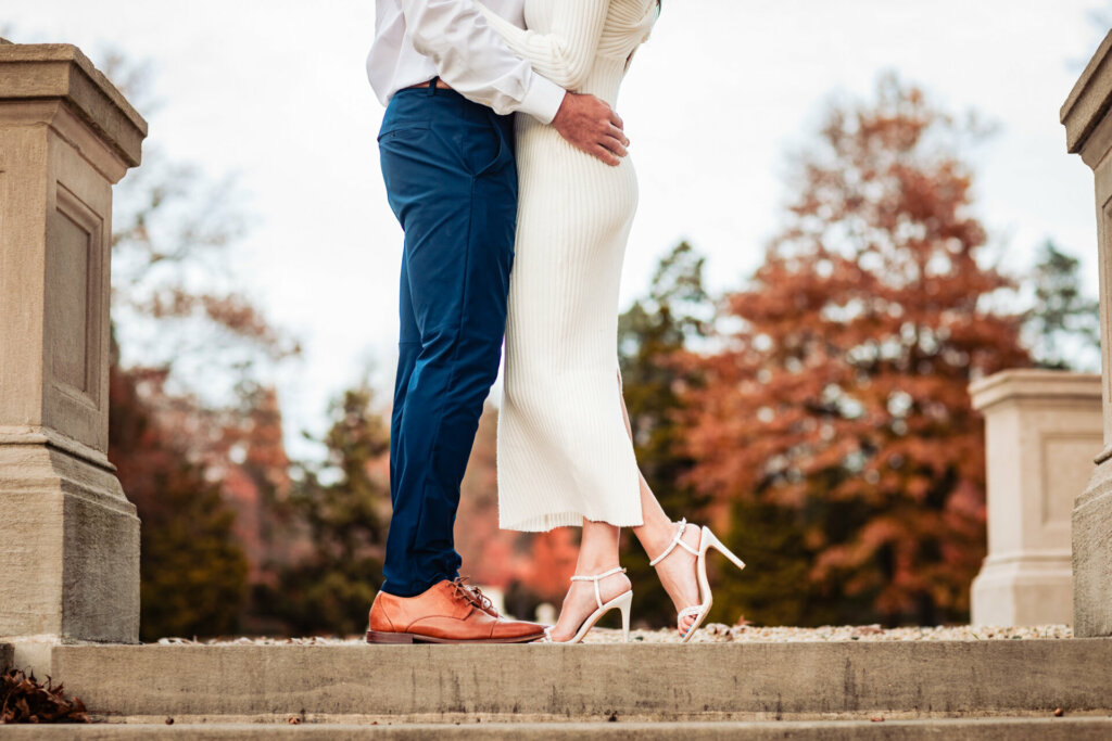 In this close-up shot, the focus is on the lower bodies of the couple. The man's hand gently rests on the woman's back as she lifts up one of her high heels, capturing a subtle and intimate moment in their connection and shared joy.